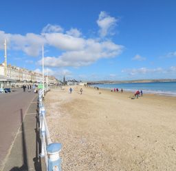 A sandy beach with people walking near the water and a row of buildings along a promenade at Day Cottage in Weymouth