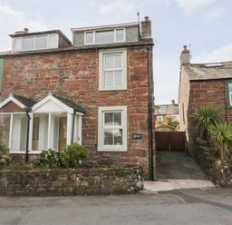 A stone house with green window frames and small garden in front at Wainwright Cottage in Gosforth