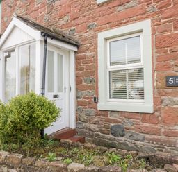 The exterior of a stone cottage with a white door porch and a window beside a small garden at Wainwright Cottage in Gosforth
