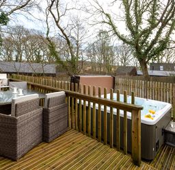 An outdoor deck with a glass table surrounded by four chairs a hot tub with drinks on the side and trees in the background at Lodge 3 in Corfe Castle