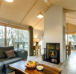 A living room with a grey sofa and wooden coffee table near a wood burning stove and dining area at Lodge 3 in Corfe Castle