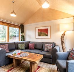 A living room with a grey sofa and armchair a wooden coffee table with a puzzle and large windows at Lodge 9 in Corfe Castle