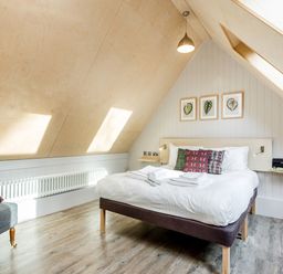 A bedroom with a double bed sofa framed leaf prints and slanted wooden ceiling at Lodge 9 in Corfe Castle