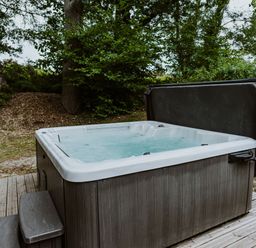 An outdoor hot tub with steps on a wooden deck surrounded by trees and greenery at Lodge 11 in Corfe Castle
