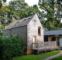 A wooden cabin with a small fenced deck and pathway surrounded by trees at Lodge 12 in Corfe Castle