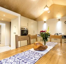 A kitchen with wooden dining table and chairs a flower vase and a wooden bowl on the table at Lodge 13 in Corfe Castle