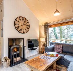 A living room with a wooden coffee table with a jigsaw puzzle on it a gray sofa a wall clock a fireplace and large windows at Lodge 13 in Corfe Castle