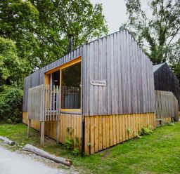 Two small wooden cabins with vertical paneling surrounded by grass and trees at Lodge 17 in Corfe Castle