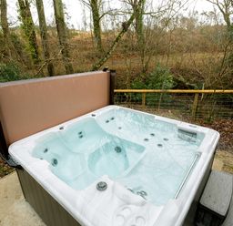 An outdoor hot tub with water and cover open next to a fence with trees behind at Lodge 19 in Corfe Castle