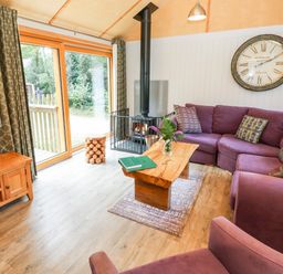 A living room with a purple sectional sofa and armchair a wood burning stove and a wooden coffee table at Lodge 21 in Corfe Castle