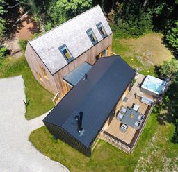 A wooden house with a black-roofed extension a deck with outdoor furniture and a hot tub surrounded by grass and trees at Lodge 22 in Corfe Castle