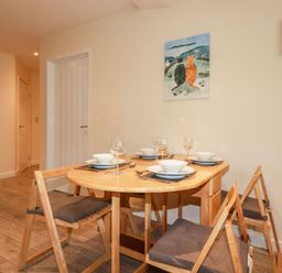 A dining area with a wooden table set for four and four wooden chairs with cushions at Falcon House in Tintagel