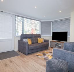 A living room with two gray sofas a television on a wooden stand and a rug at Falcon House in Tintagel