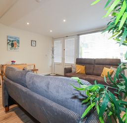 A living room with two sofas, a small table with chairs, wall art, and a large window with blinds at Falcon House in Tintagel