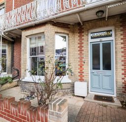 An exterior view of a brick townhouse with a blue front door labeled ELKHORN and a small front garden with plants in Southwold
