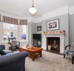 A living room with striped armchairs a wooden coffee table a fireplace and a television at Elkhorn in Southwold