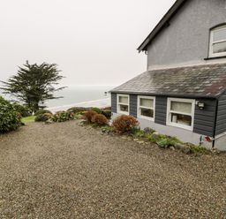A gravel driveway next to a house with windows overlooking trees and the sea at Sibrwd Y Mor in Harlech