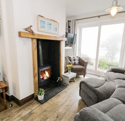 A living room with a fireplace armchair sofa and sliding glass doors at Sibrwd Y Mor in Harlech