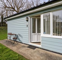 Exterior view of a light blue building with a half-open door and a small wooden table with two chairs on a concrete patio at 11 The Dell in Mundesley