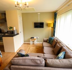 A living room with a brown sofa and a wall mounted tv next to an open kitchen at 11 The Dell in Mundesley