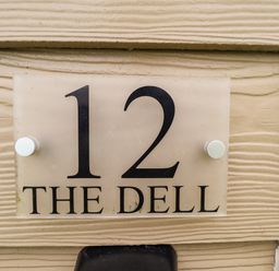 A house number sign with 12 and the name The Dell on a beige textured wall at 12 The Dell in Mundesley