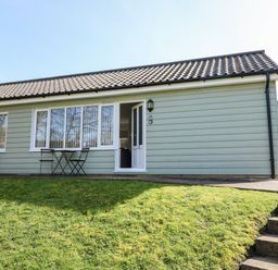 Exterior view of a single-story building with green siding small tables and chairs outside at 14 The Dell in Mundesley