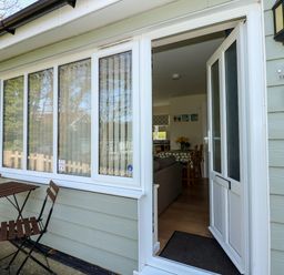 A small outdoor patio with a table and two chairs and a partially open door leading into a dining area at 14 The Dell in Mundesley