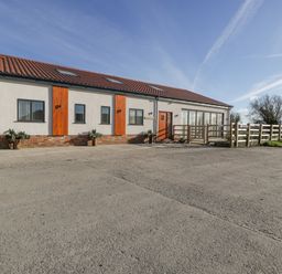 A single story building with tiled roof wooden door and windows next to a fence and open area at Bilsham Meadows in Aust