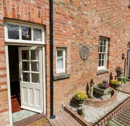 An open white door on a brick wall with the number 4 above it and a garden area with plants at 4 The Old Council House in Shipston-On-Stour