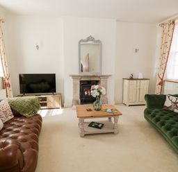 A living room with two sofas a wooden coffee table a fireplace a television and floral curtains at 4 The Old Council House Shipston-On-Stour