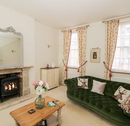 A living room with a green sofa, wooden coffee table, stone fireplace, and floral curtains at 4 The Old Council House in Shipston-On-Stour