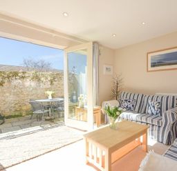 A living room with striped sofas a wooden coffee table and open doors leading to a patio with outdoor furniture at Smugglers Cove 7 in Beadnell