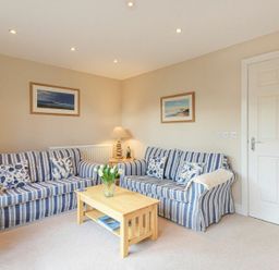 A living room with two striped sofas and a wooden coffee table with flowers at Smugglers Cove 7 in Beadnell