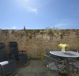 An outdoor patio with two black reclining chairs a round metal table with four chairs and a vase with flowers at Smugglers Cove 7 in Beadnell