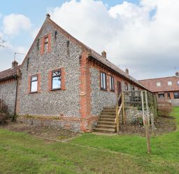 A stone and brick building with wooden stairs and green grass at Timbers in Weybourne