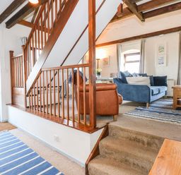 An interior room with wooden staircase blue sofas a brown armchair striped rugs and windows at Timbers in Weybourne