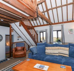 A living room with a blue sofa brown armchair wooden coffee table and visible wooden beams at Timbers in Weybourne