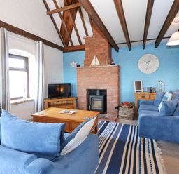 A living room with blue sofas a brick fireplace a wooden coffee table and a TV at Timbers in Weybourne