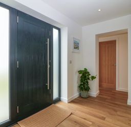 An entryway with a black front door wooden flooring a brown mat a plant in a pot and a closed wooden interior door at Refail Fach Near Cemaes Bay