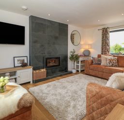 A living room with a fireplace a large rug and brown sofas at Refail Fach Near Cemaes Bay