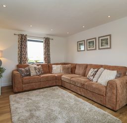 A living room with a large brown sectional sofa cushions patterned curtains and framed pictures on the wall at Refail Fach Near Cemaes Bay