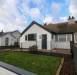 A white semi detached house with a fenced front yard and grass in Llanfairpwllgwyngyll