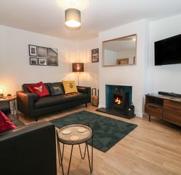 A living room with two black sofas colorful cushions fireplace TV on wooden cabinet and dark rug at Ty Nain in Llanfairpwllgwyngyll