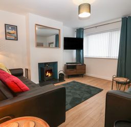 A living room with two black sofas a fireplace a wall mounted tv and a wooden cabinet at Ty Nain in Llanfairpwllgwyngyll