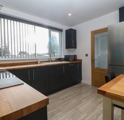 A kitchen with wooden countertops a stainless steel refrigerator a wooden door and a table with chairs at Ty Nain in Llanfairpwllgwyngyll