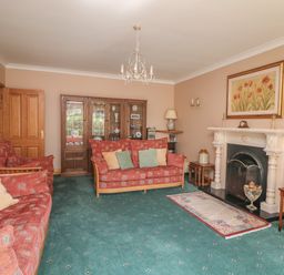 A living room with two red patterned sofas a fireplace with a painting above and a wooden cabinet at Bolger House Ballintubbrid near Kilmuckridge County Wexford