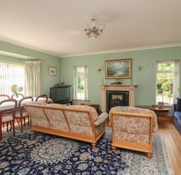 A living room with floral sofas a blue rug a dining table and chairs a fireplace and a television at Bolger House Ballintubbrid near Kilmuckridge County Wexford