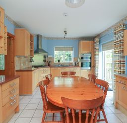 A kitchen with a wooden dining table and chairs light wood cabinets blue walls and striped curtains at Bolger House in Ballintubbrid near Kilmuckridge County Wexford