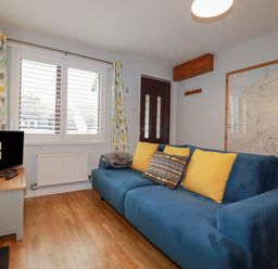 A living room with a blue sofa with yellow cushions a wooden floor a small TV on a table a window with patterned curtains and a wall map at Bumbles in Padstow