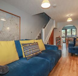 A living room with blue sofas and yellow cushions near a staircase and dining area at Bumbles in Padstow